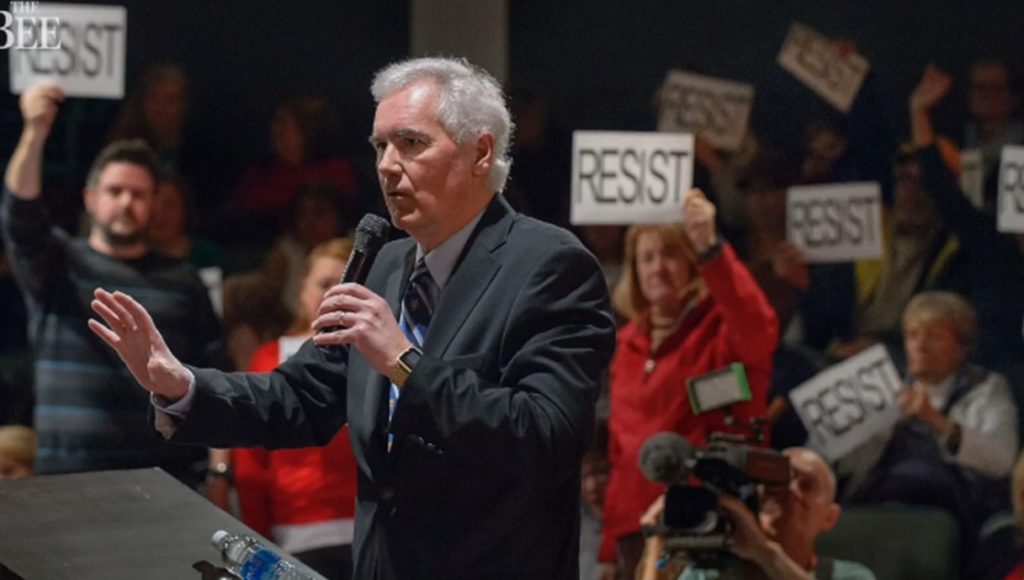 Strangely perfect pre-printed signs come out at CA Rep. Tom McClintock's recent townhall in Roseville. (Image: Screen grab of Sacramento Bee video via San Jose Mercury News)
